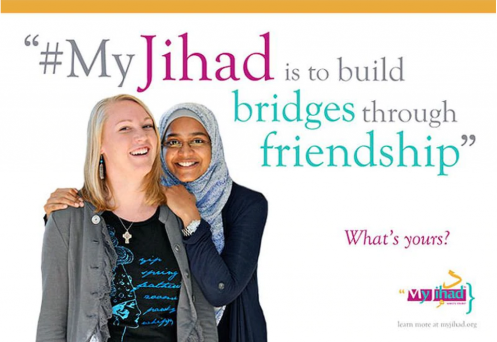 A white woman wearing a t-shirt and cardigan stands in front of a brown-skinned woman wearing a hijab, whose hands are on the white woman's shoulders. Both women are smiling broadly. Above and to the side of the women, multicolored text reads "#MyJihad is to build bridges through friendship. What's yours?"